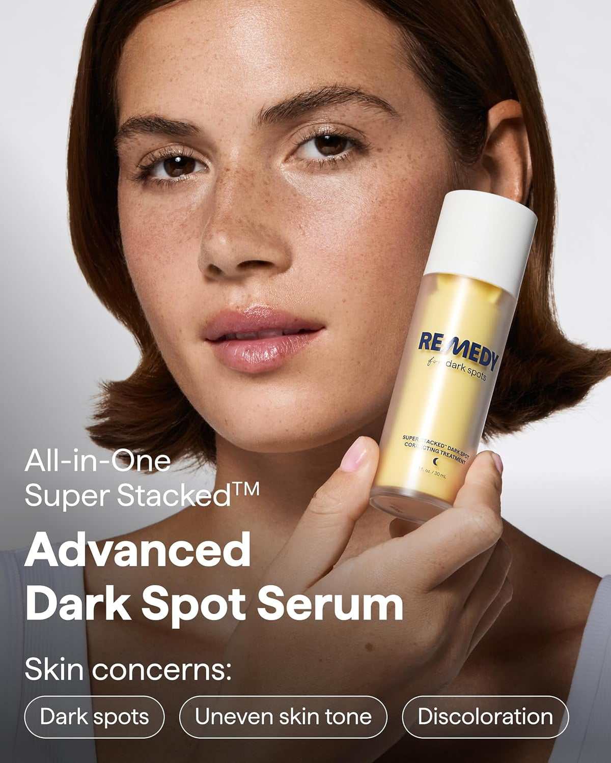Advanced dark spot serum bottle held beside face for uneven skin tone