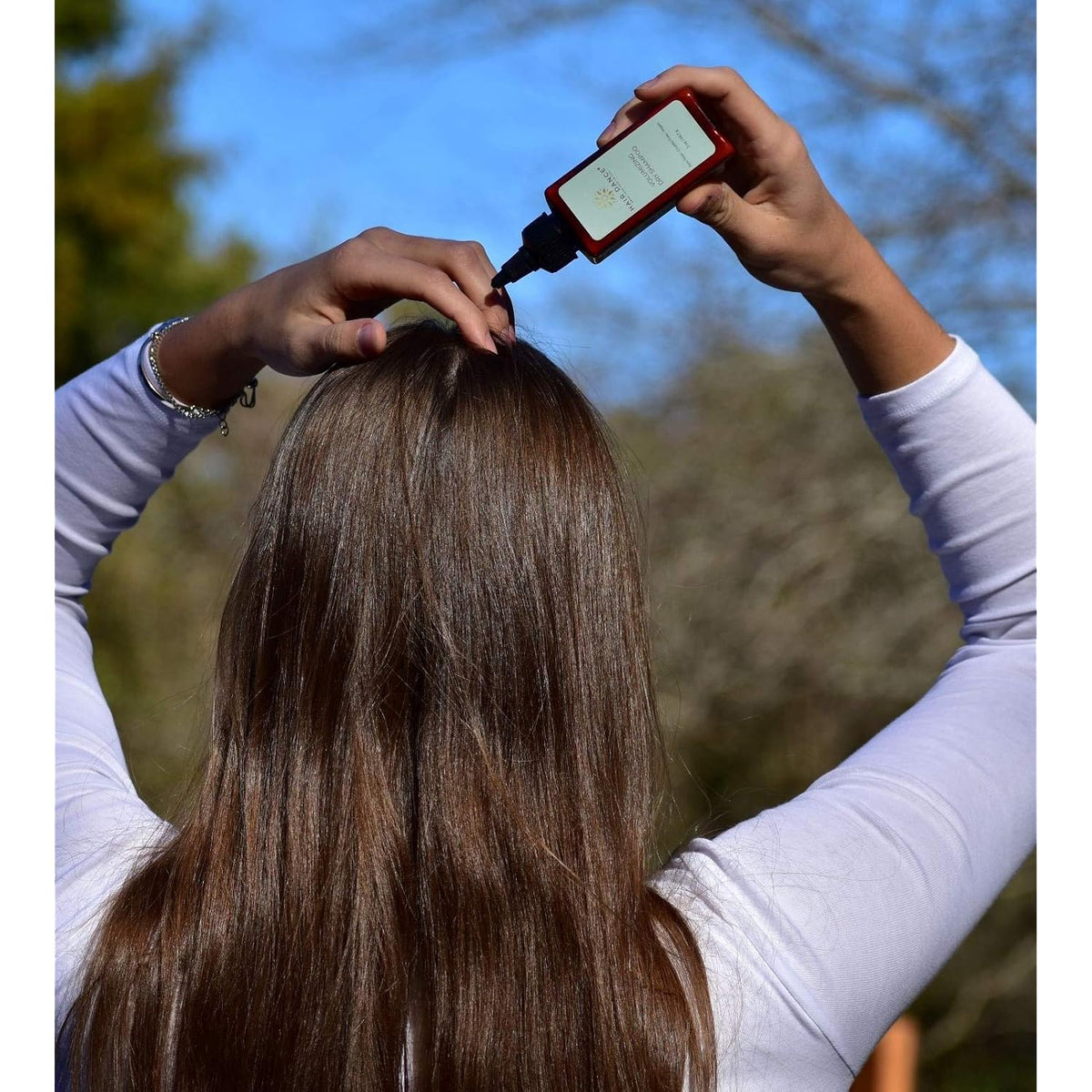 Hands holding dry shampoo bottle above hair, applying volumizing product