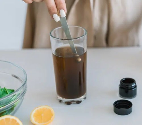 Glass of brown drink with spoon; small shilajit jar bottles nearby