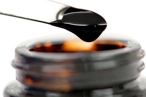 Open jar of dark shilajit resin with black spoon