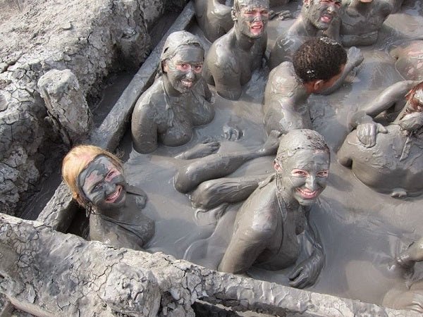 Mud bath scene with people covered in gray-black mud in a rocky pool