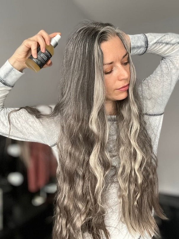 Woman spraying thickening treatment onto long wavy gray hair with a pump bottle