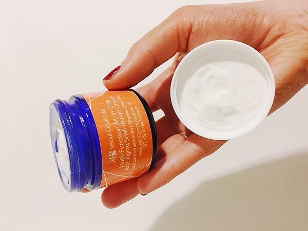 Hand holding a small snail repair cream jar with white cream shown
